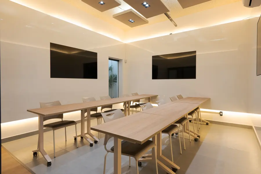 Sala com duas mesas longas, cadeiras e telas